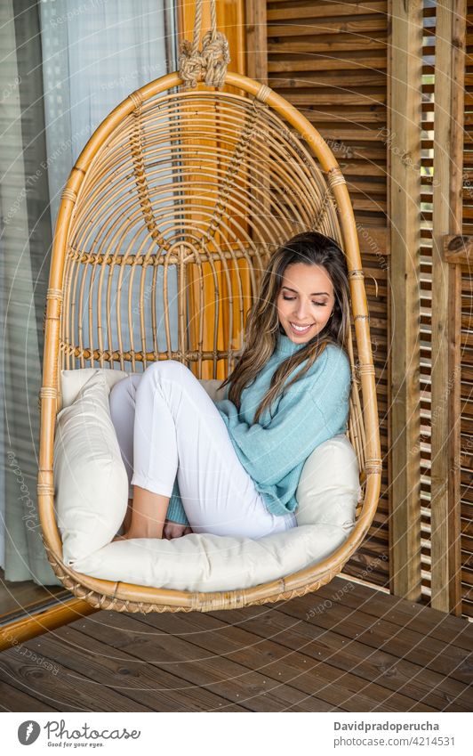 Cheerful woman resting in wicker hanging chair chill natural wooden happy style enjoy furniture rattan cushion comfort home smile cheerful design charming
