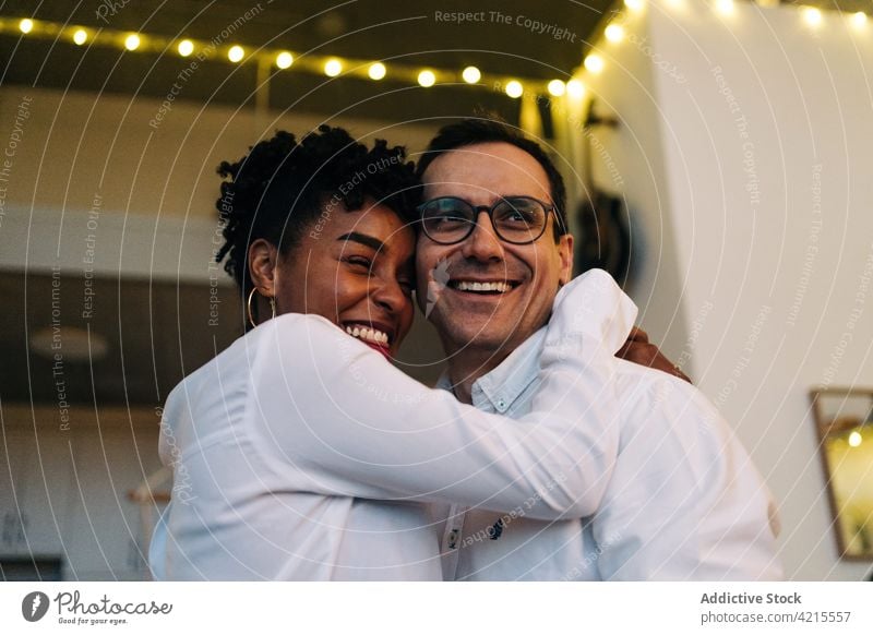 Happy multiethnic couple embracing in cozy room at home hug romantic garland light fairy light cheerful love evening multiracial diverse black african american