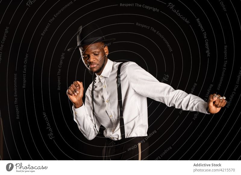 Stylish black man in white shirt and hat dancing on black background model style fashion well dressed gentleman happy dance masculine portrait macho garment