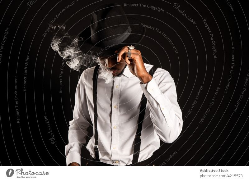 Stylish ethnic man vaping on black background vape e cigarette smoke nicotine exhale style masculine diffuse portrait fashion individuality macho virile spread