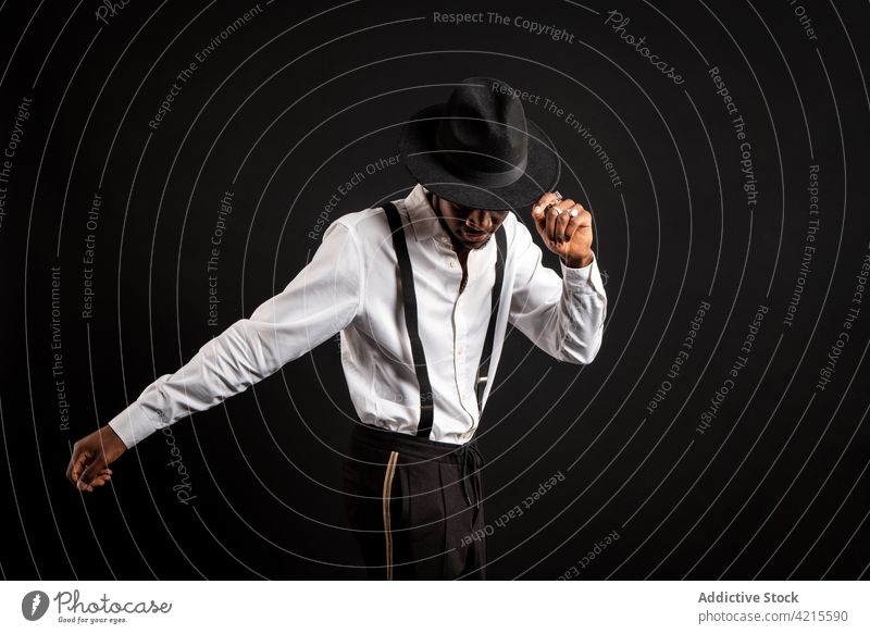 Stylish black man in white shirt and hat dancing on black background model style fashion well dressed gentleman happy dance masculine portrait macho garment