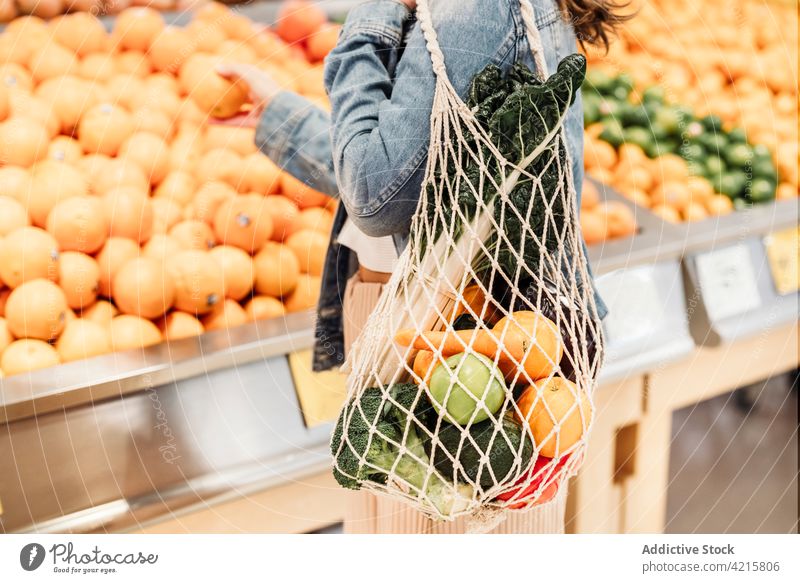 Crop woman with fresh groceries in mesh bag in supermarket eco friendly grocery buyer zero waste fruit vegetable female food ripe shopper store counter stall