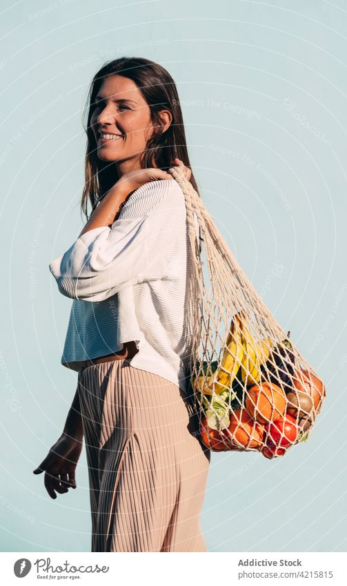 Cheerful woman with mesh bag full of ripe groceries grocery cotton food eco friendly zero waste fruit vegetable female smile cheerful content healthy food