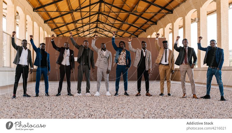 Black businessmen in suits with raised arms fist up style fashion rebel revolution self assured portrait building hand in pocket black power solidarity