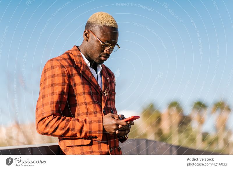Trendy black man texting on smartphone in town fashion tartan style checkered blond using gadget african american device ethnic individuality ornament masculine