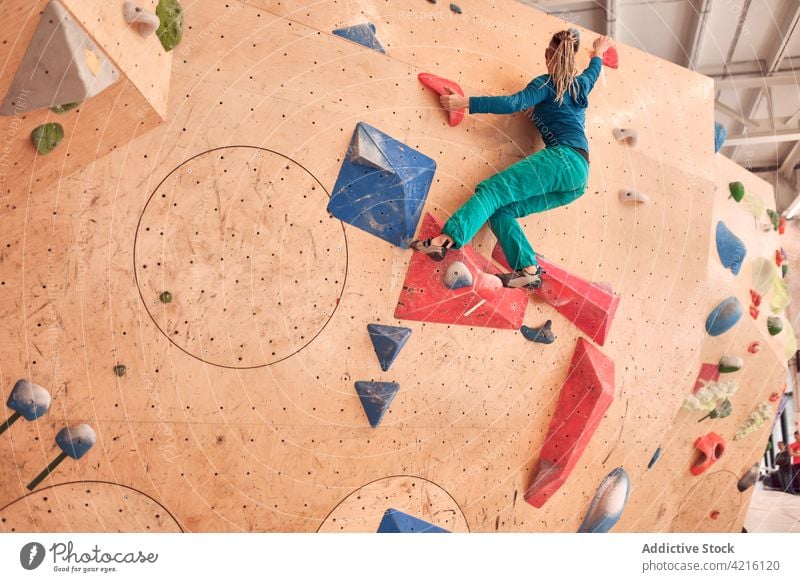 Unrecognizable female climber ascending wall in bouldering gym sportswoman hang training mountaineer alpinist strong workout exercise balance grip extreme