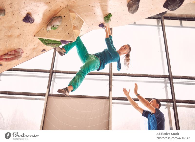Sportswoman climbing wall in bouldering center sportswoman training balance strong instructor supervise extreme trainer mountaineer exercise climber strength