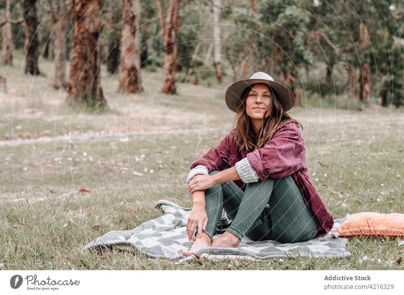 Content woman sitting on blanket in forest during picnic content enjoy meadow carefree plaid summer female australia happy smile nature delight environment park