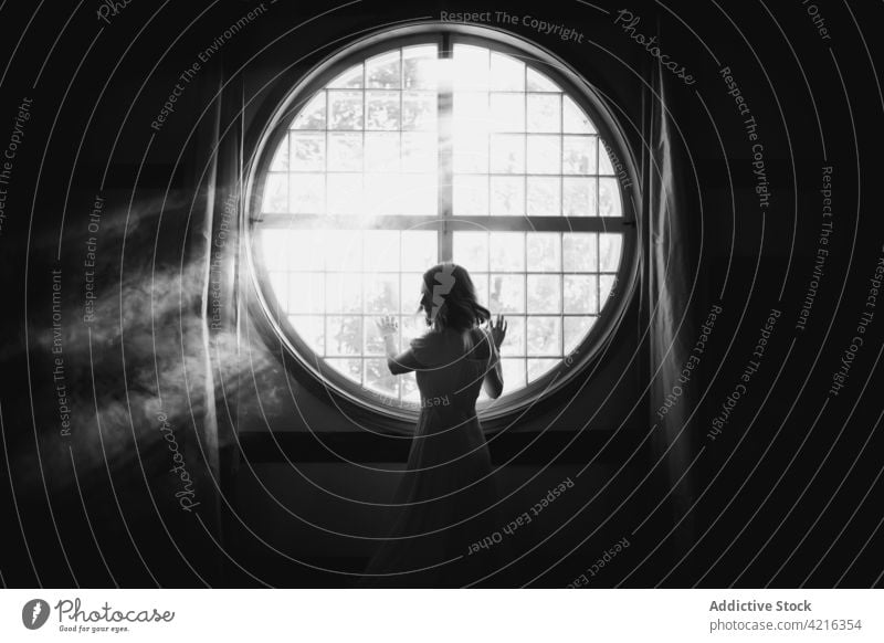 Anonymous woman looking out window at home in sunshine look out solitude gentle magic tender feminine house romantic idyllic sunbeam geometry air sunlight