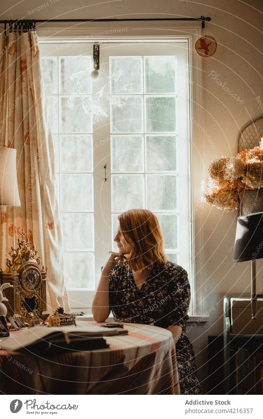 Dreamy woman at table with antique clock at home dreamy decor book window idyllic harmony house enjoy mindfulness retro style plant shiny decoration literature