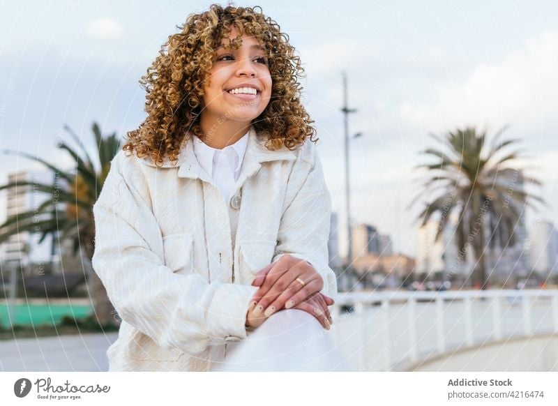 Happy black woman standing near fence in city tropical evening carefree dreamy enjoy smile street female ethnic african american afro curly hair relax charming