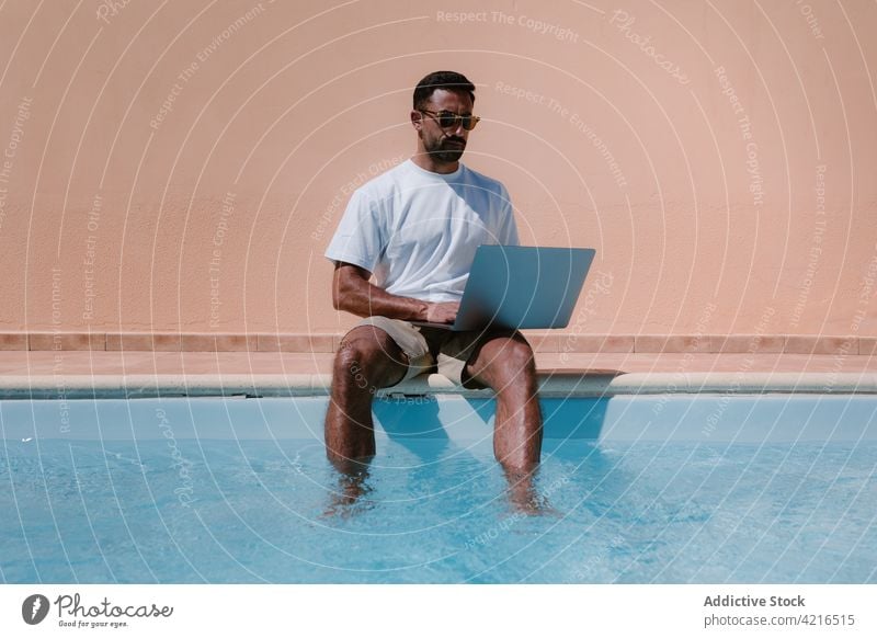 Man using laptop at poolside freelance typing man work telework remote summer male vacation internet online resort surfing browsing travel computer netbook