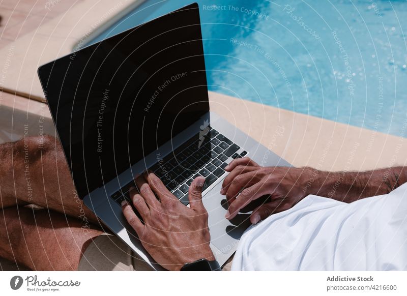 Anonymous man lying on deckchair and browsing on computer near pool freelance poolside telework summer lounger male internet online using remote gadget vacation