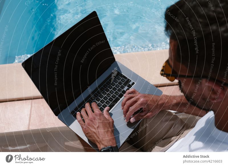 Man lying on deckchair and browsing on computer near pool man freelance poolside telework summer lounger male internet online using remote gadget vacation