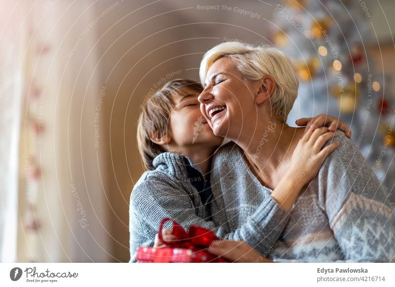 Son giving mother Christmas gift son boy child children kids hugging embracing winter christmas christmas tree lifestyle indoors happy people Caucasian fun joy