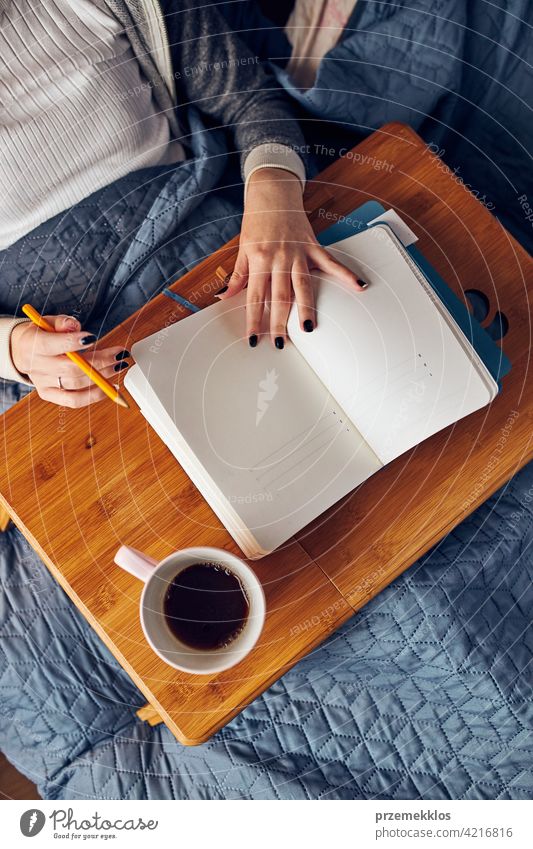 Student learning at home. Young woman making notes, reading and learning from notepad. Girl writing journal sitting in bed education indoor student working