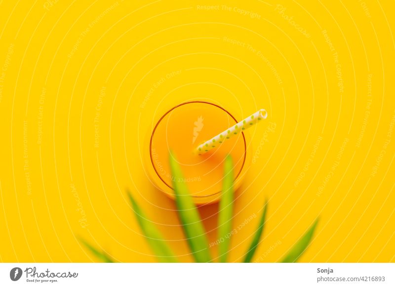 A glass of orange juice with a straw and a palm leaf on a yellow background. Top view Orange juice Palm leaf plan Beverage Summer Glass Refreshment Cold drink