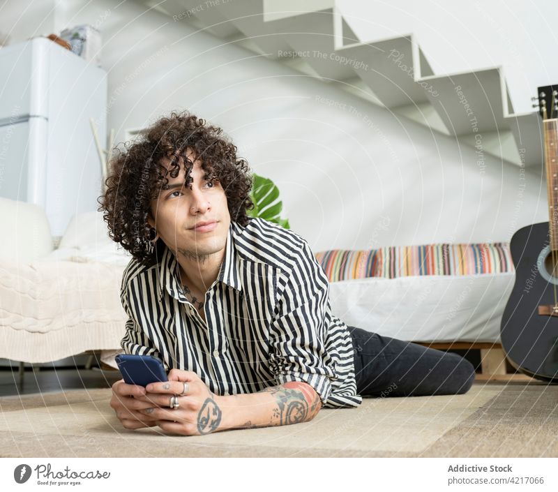 Dreamy man with smartphone resting on floor in house dreamy tattoo ponder friendly sincere spare time portrait guitar acoustic music classic stair home hipster