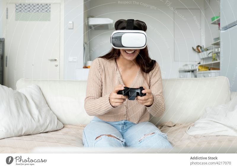 Anonymous gamer in VR headset with game console indoors play videogame gamepad vr goggles entertain woman home using gadget immerse device cheerful controller