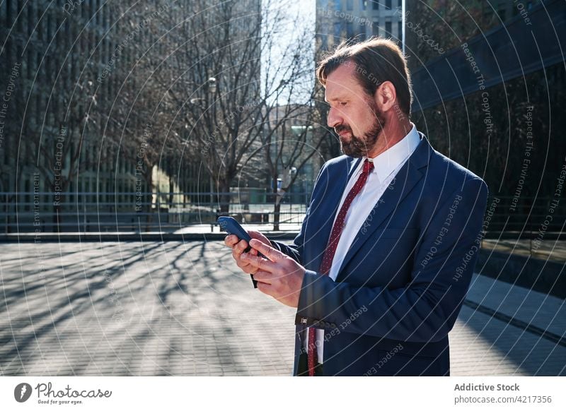 Businessman browsing smartphone in city businessman executive manager surfing downtown entrepreneur using male mobile gadget serious professional suit device