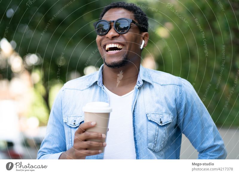 Man holding a cup of coffee. african american man street sunglasses city urban concept walking ear buds ear pods smile take away leisure beverage enjoy earbud
