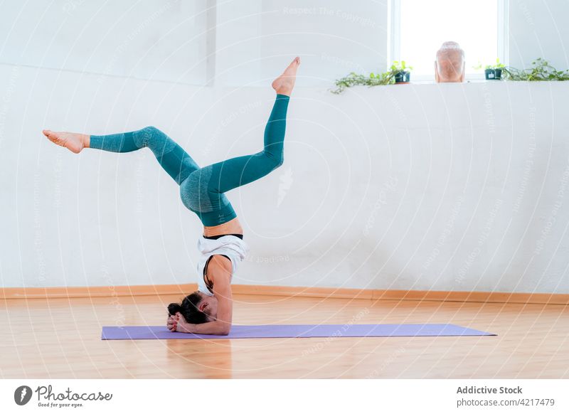 Unrecognizable woman performing Supported Headstand with Splits pose in room headstand legs raised balance yoga inversion talent skill practice house perfect