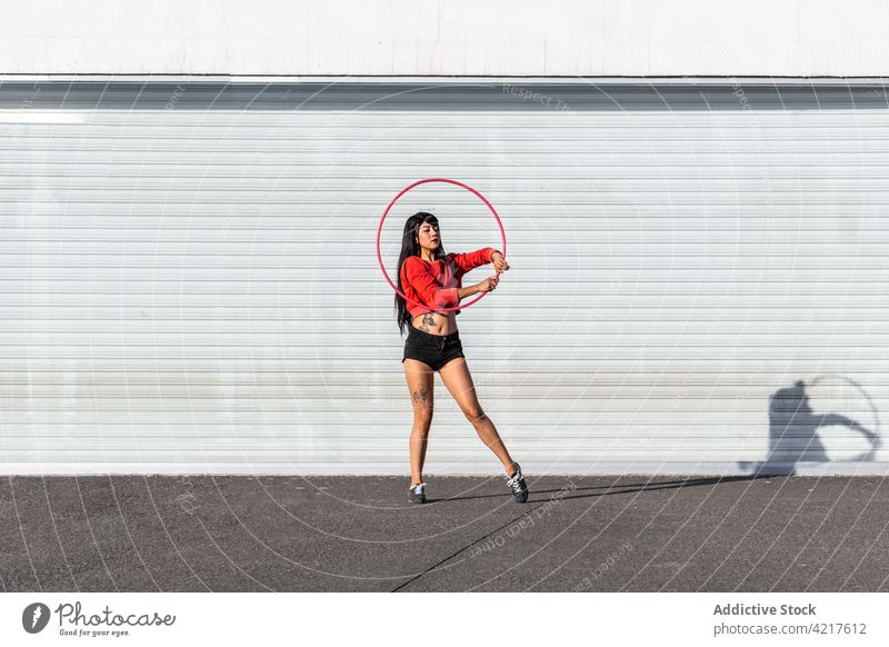 Dancer spinning hula hoop on pavement dancer active fit tattoo woman twirl movement choreography shadow body confident sportswear sneakers equipment asphalt