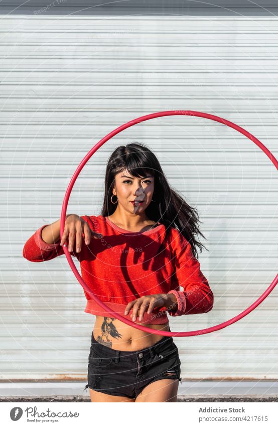 Dancer spinning hula hoop on pavement dancer active fit tattoo woman twirl movement choreography shadow body confident sportswear sneakers equipment asphalt