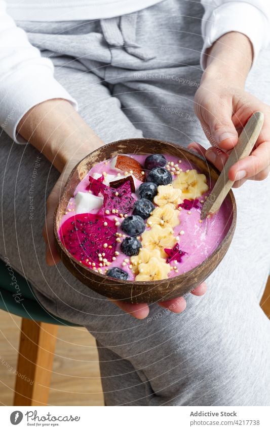 Crop woman with delicious breakfast bowl full of fruits power bowl healthy food smoothie nutrient vitamin exotic yummy ripe legs crossed tasty organic fresh