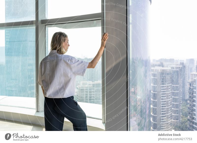 Lonely girl in empty office watching cityscape beautiful black pants blond bright building casual caucasian copy space day emotions empty room fashion female
