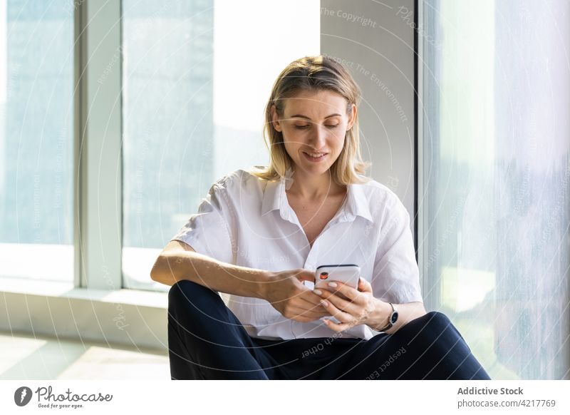 Woman in empty office using a smartphone woman black pants blond happy smile building thoughtful caucasian cell phone copy space delight device mobile browsing