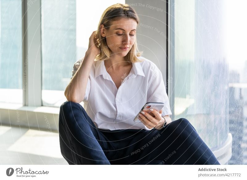 Woman in empty office using a smartphone woman black pants blond bright building thoughtful caucasian cell phone copy space device mobile browsing young sit