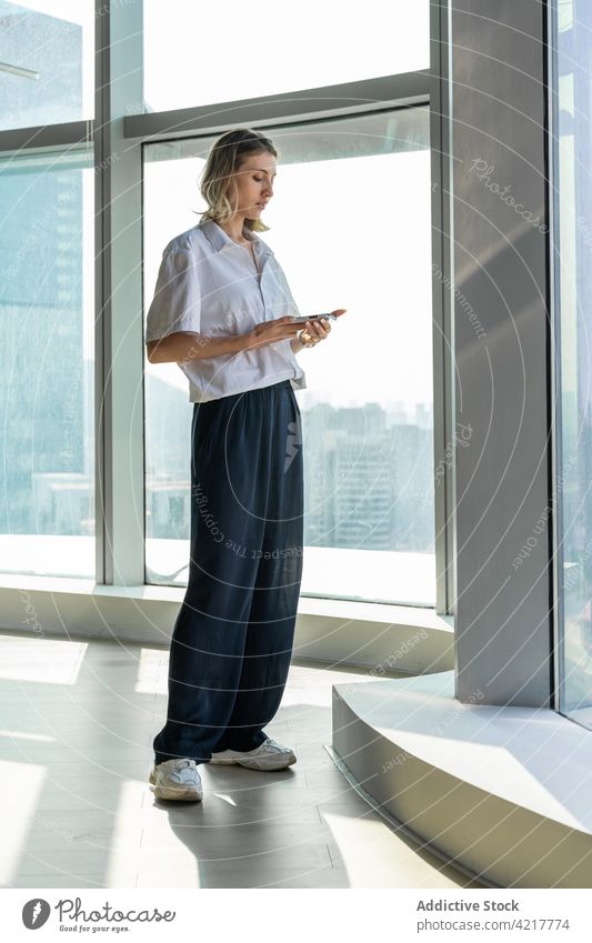 Woman in empty office using a smartphone woman black pants blond bright building thoughtful caucasian cell phone copy space device mobile browsing young
