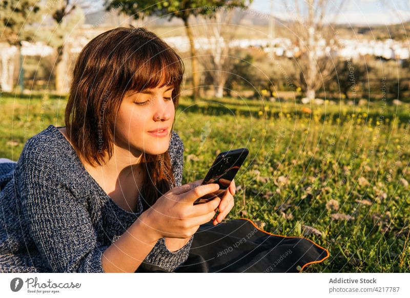 Woman lying on blanket during picnic in park woman spring smartphone using meadow sunny enjoy dreamy carefree female relax nature rest device field weekend