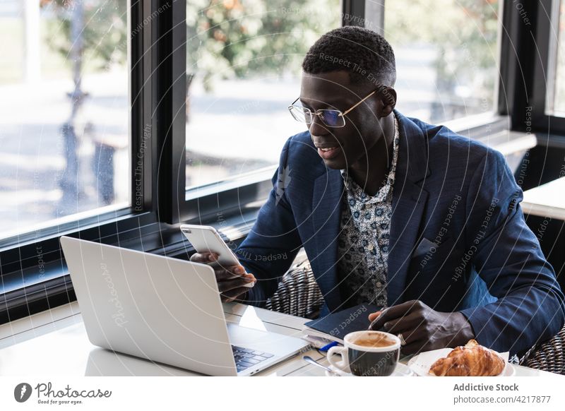 Stylish ethnic executive with smartphone and laptop in cafe work chatting well dressed breakfast man using gadget device cellphone watching eyeglasses
