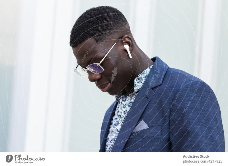 Content black businessman listening to music in earbuds in city style downtown well dressed entrepreneur content male ethnic african american street urban