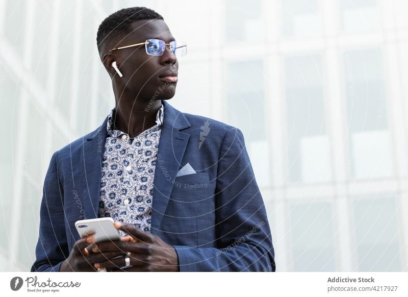 Stylish black entrepreneur in earbud with smartphone businessman well dressed self employed masculine contemplate multimedia portrait using gadget device