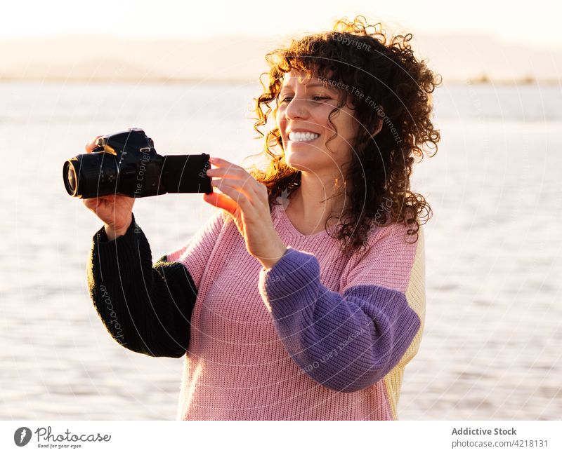 Happy woman with photo camera on beach sea happy traveler check cheerful photography nature female smile ethnic vacation tourist holiday positive enjoy