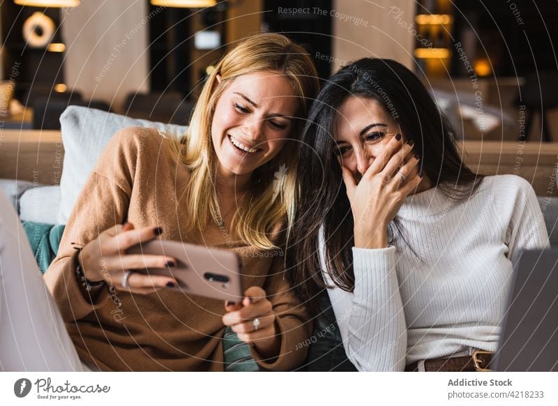 Cheerful lesbian women watching funny video on smartphone couple laugh having fun entertain female using gadget cheerful girlfriend device sofa sit lgbt lgbtq