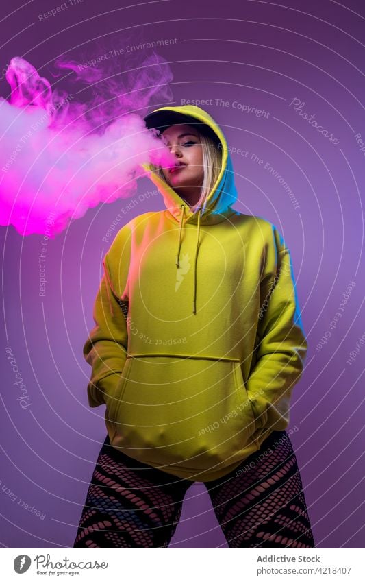 Trendy woman in hoodie smoking vape in studio smoke e cigarette fume cool street style hipster female nicotine habit unhealthy fashion exhale posture