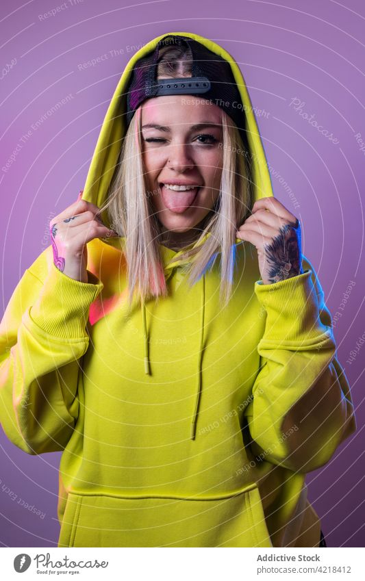 Cheerful woman in hoodie showing tongue in studio show tongue hipster rebel tongue out face expression make face grimace neon light female trendy individuality