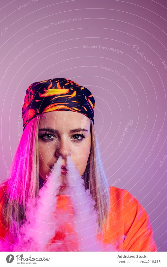 Woman smoking vape in studio with neon lights woman smoke e cigarette cool street style fume female nicotine habit unhealthy fashion exhale illuminate
