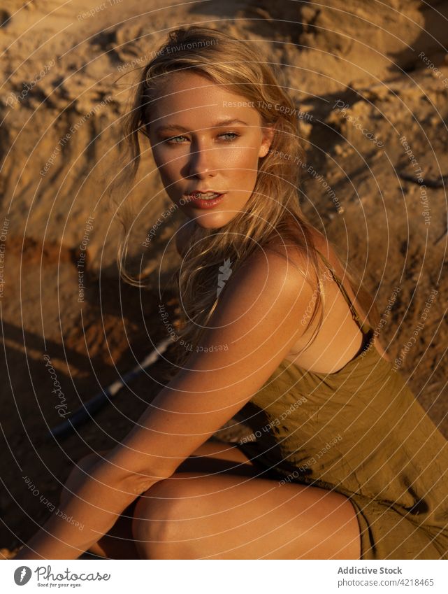 Young woman sitting on sandy ground in evening nature slope peaceful posture carefree harmony natural tranquil female serene blond vegetate recreation young