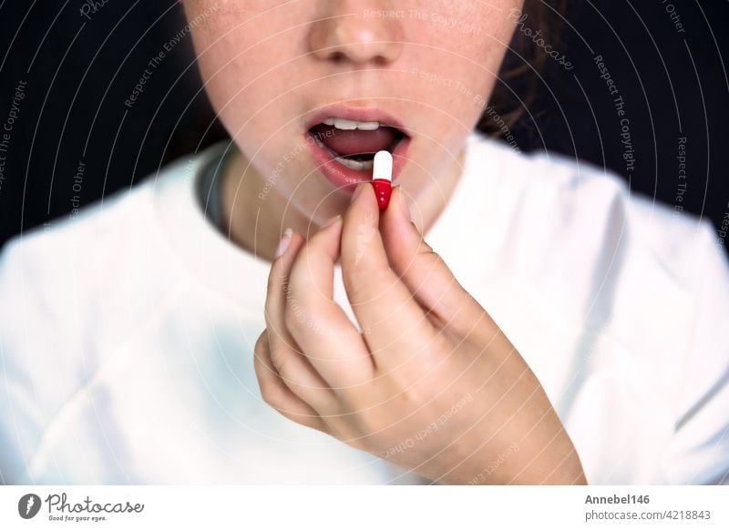 Young woman,teenager with Capsule on tong on dark black background, taking pills. medicine,drugs,health concept medical design love food person girl junky face