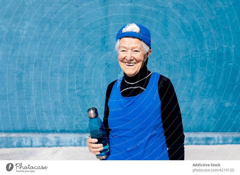 Joyful senior sportswoman with water bottle in outdoor sports center toothy smile activewear vitality fitness mature motivation energy lifestyle sportswear