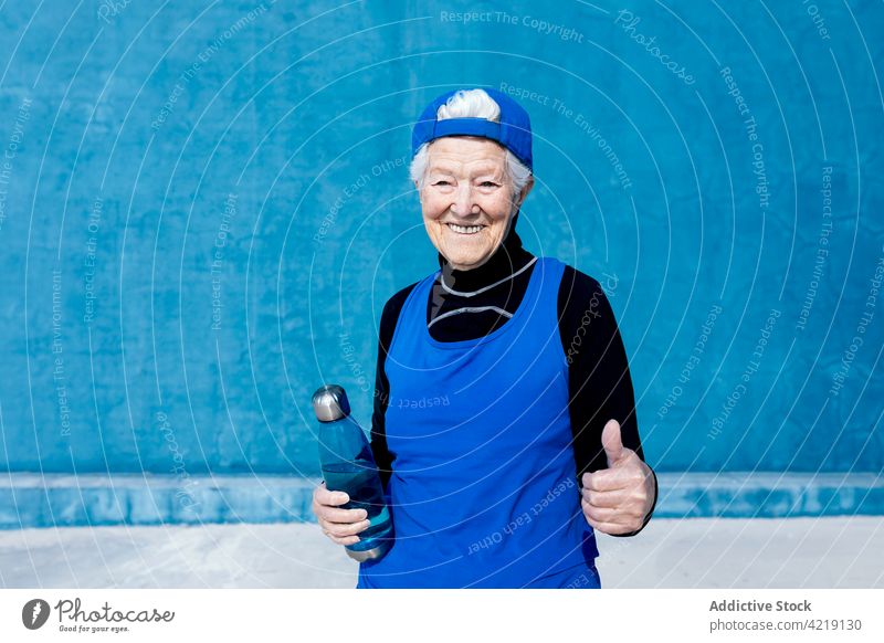 Joyful senior sportswoman with water bottle in outdoor sports center toothy smile activewear vitality fitness mature motivation energy lifestyle sportswear