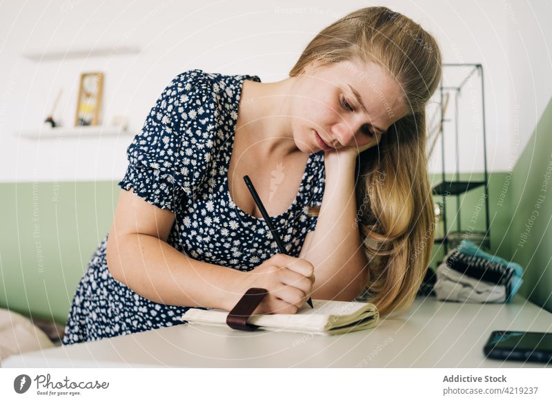Woman writing in notebook at table in house woman take note lean on hand attentive feminine gentle portrait pen write paper notepad natural smartphone gadget