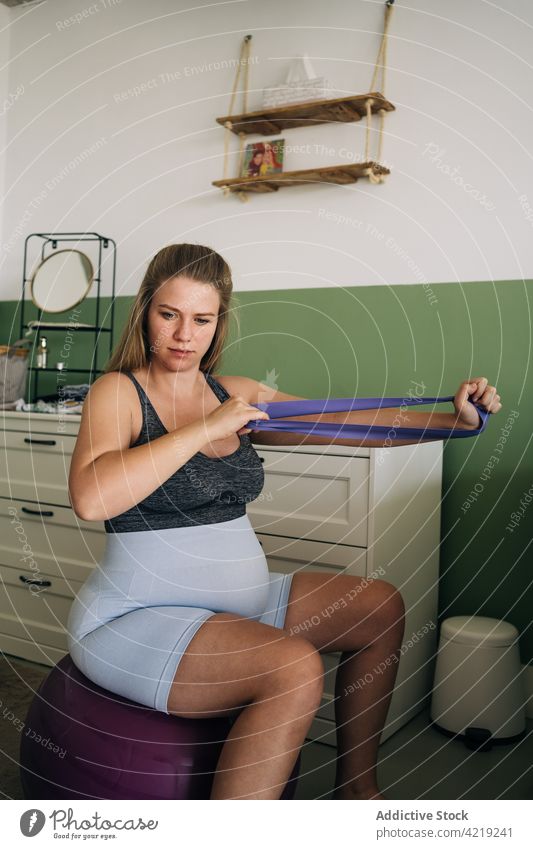 Pregnant woman on yoga ball working out with elastic band resistance band exercise pregnant workout sport training maternal home practice fitness belly
