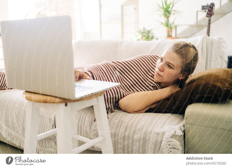 Tired woman watching film on laptop while resting on sofa movie weekend spare time tired using gadget device home plaid stripe ornament cushion soft lounge