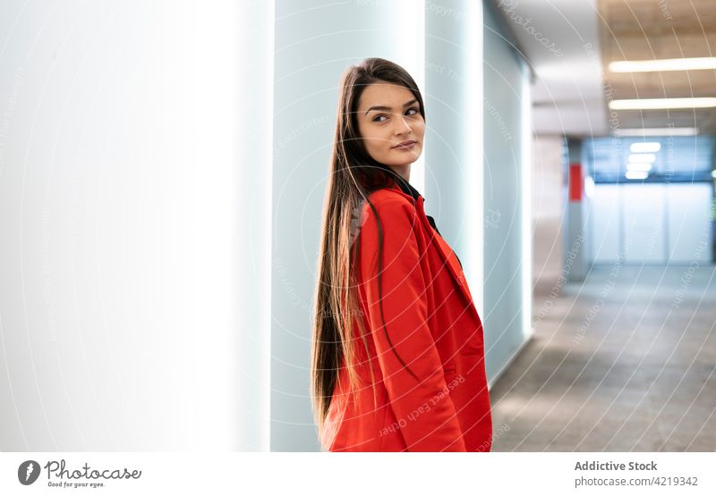 Trendy woman standing near illuminated wall in shopping center mall style trendy outfit glow female hallway corridor passage shopper cheerful smile happy